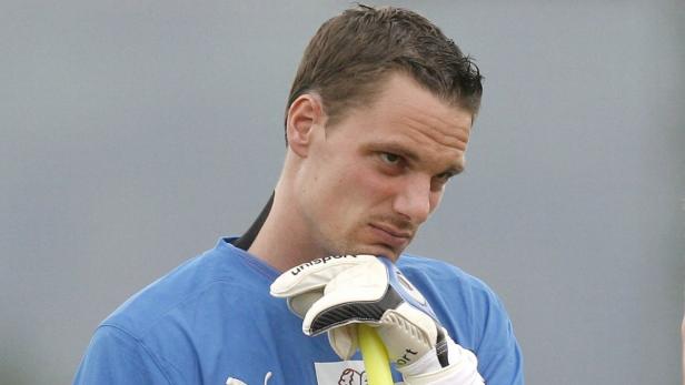 Ein Torwart in blauem Trikot und Handschuhen blickt nachdenklich zur Seite.