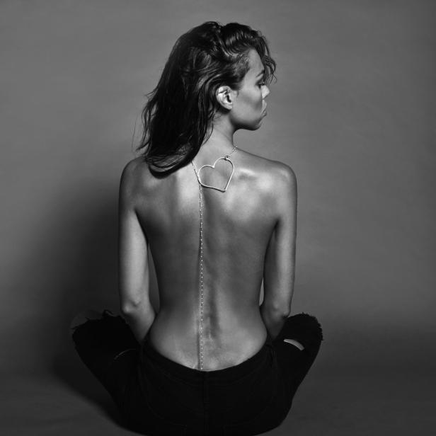 Eine Frau sitzt mit dem Rücken zur Kamera, eine Herzkette auf dem Rücken tragend.