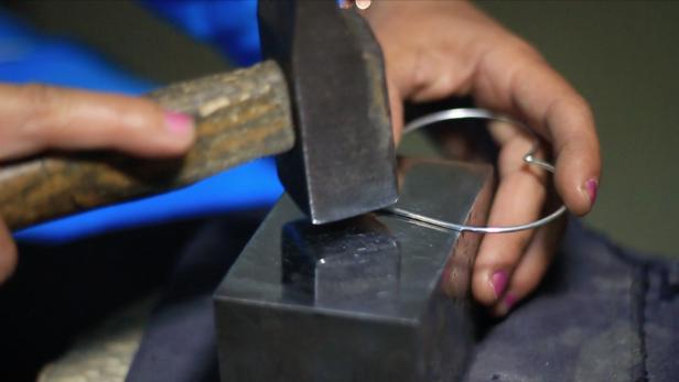 Eine Person formt mit einem Hammer einen silbernen Armreif.