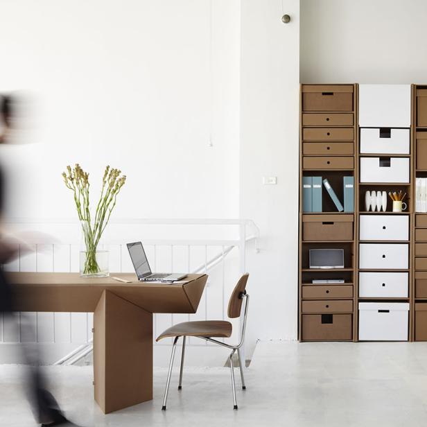 Ein minimalistisches Büro mit Pappmöbeln und einem Laptop auf dem Schreibtisch.