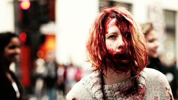 Eine als Zombie verkleidete Person mit blutverschmiertem Gesicht auf einer Straße.