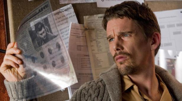 Ethan Hawke betrachtet nachdenklich einen Zeitungsartikel an einer Pinnwand.