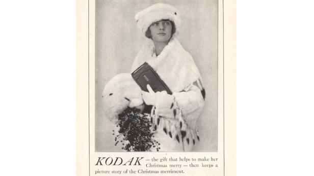 Eine Frau in Winterkleidung hält eine Kamera und einen Mistelzweig.