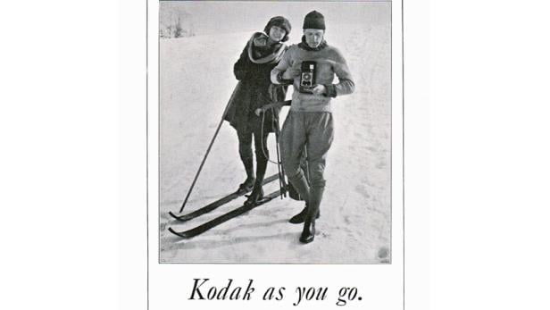Ein Paar im Schnee, wobei der Mann eine Kamera hält und die Frau Skier trägt.