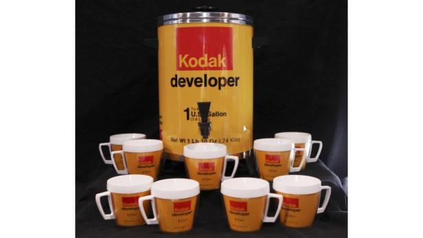 Ein Kodak-Entwicklerbehälter steht umgeben von mehreren Kodak-Entwicklertassen.