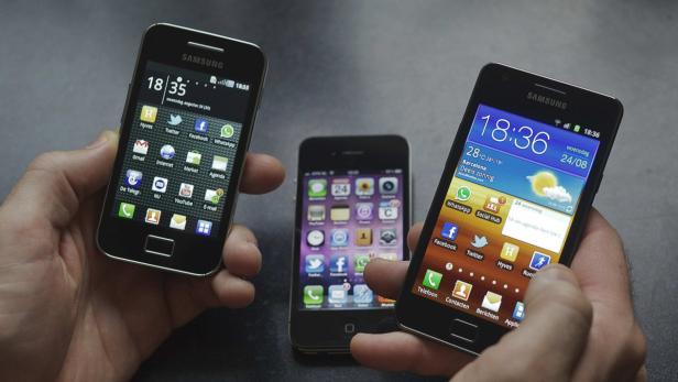 Drei Mobiltelefone, darunter ein Samsung und ein iPhone, werden von Händen gehalten.