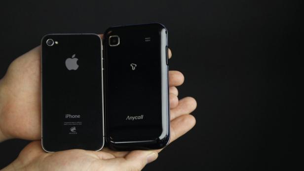 Ein iPhone und ein Anycall-Smartphone werden in einer Hand gehalten.