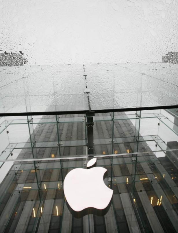 Das Apple-Logo vor einem verglasten Gebäude an einem regnerischen Tag.