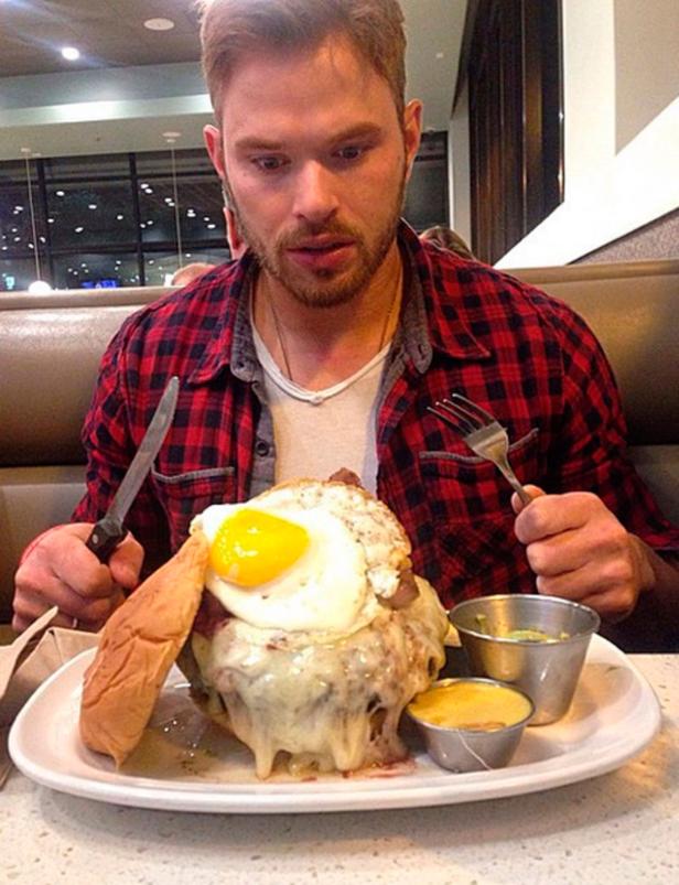 Ein Mann mit Messer und Gabel vor einem riesigen Burger mit Spiegelei.