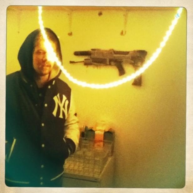 Ein Mann mit Kapuzenjacke der New York Yankees vor einer Wand mit einem Spielzeuggewehr.