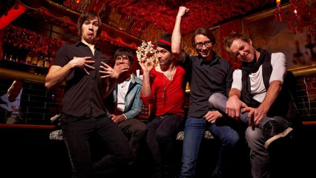 Fünf Männer posieren in einer Bar mit roter Dekoration für ein Foto.