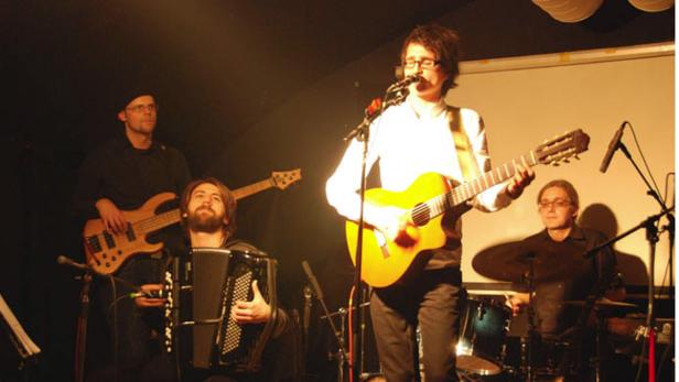 Eine Band spielt live auf einer Bühne mit Gitarre, Akkordeon, Bass und Schlagzeug.