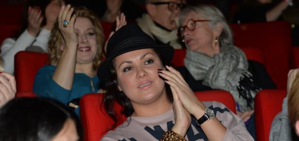 Eine Frau mit Hut sitzt im Kino, umgeben von anderen Zuschauern.
