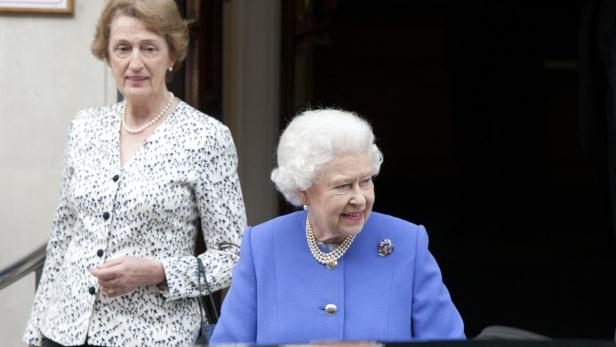 Königin Elisabeth II. in einem blauen Kostüm mit einer Begleiterin.