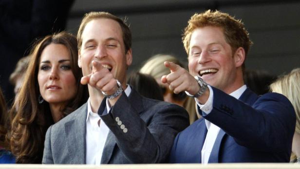 Prinz William, Kate Middleton und Prinz Harry lachen und zeigen auf etwas.