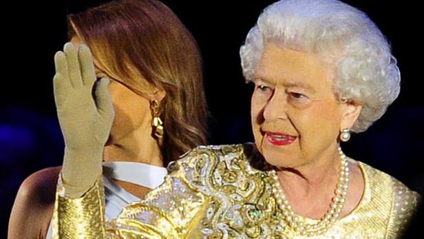 Königin Elisabeth II. in goldener Robe mit einer Frau, die ihre Hand vor ihr Gesicht hält.