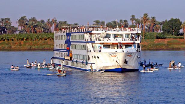 Ein großes Nilkreuzfahrtschiff mit kleinen Booten davor auf dem Wasser.