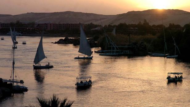 Mehrere Segelboote und Ausflugsboote fahren auf dem Nil bei Sonnenuntergang.
