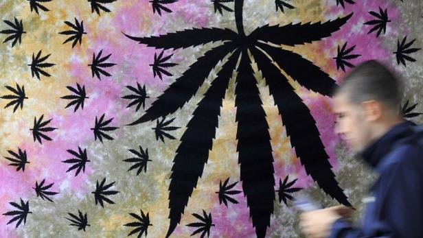 Ein Mann geht an einem Wandteppich mit einem großen Cannabisblatt-Muster vorbei.