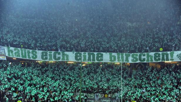 Eine große Menschenmenge schwenkt grün-weiße Fahnen hinter einem Banner mit der Aufschrift „hauts eich eine burschen!“.