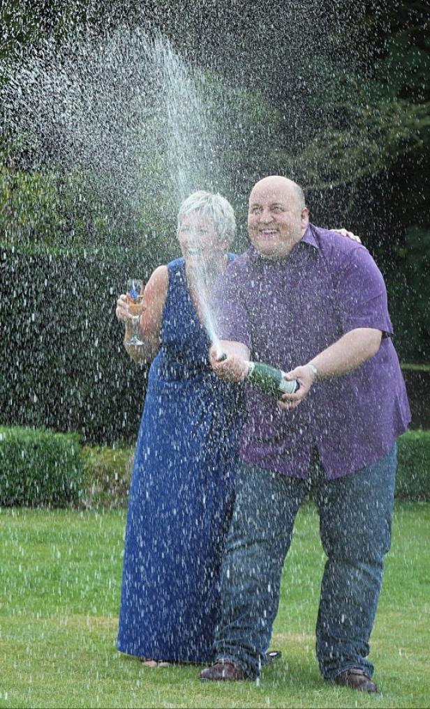 Ein Paar feiert mit einer Champagnerdusche auf einer grünen Wiese.