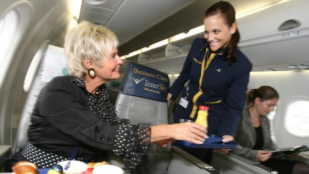 Eine Stewardess serviert einer älteren Dame ein Getränk in der Business Class eines Flugzeugs.