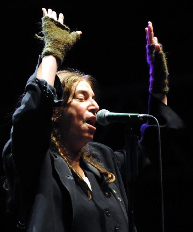 Patti Smith singt mit erhobenen Händen auf einer Bühne.