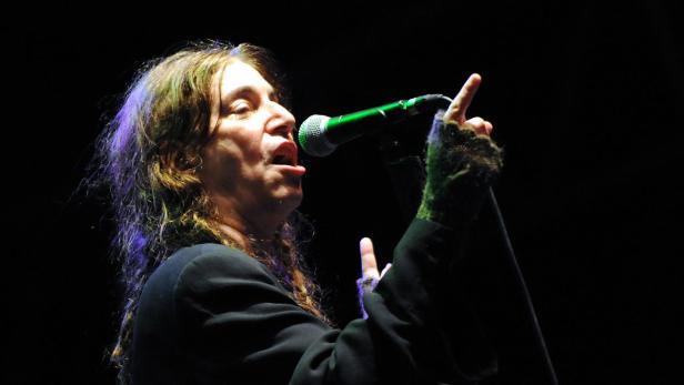Patti Smith singt mit ausgestreckter Zunge in ein Mikrofon.