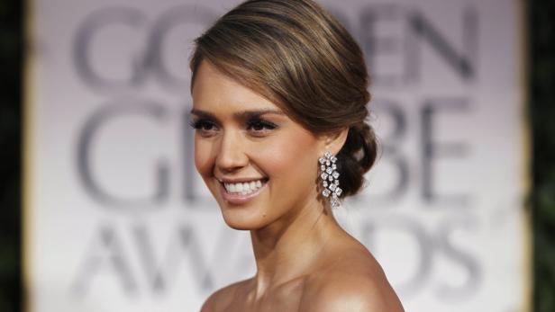 Jessica Alba lächelt mit auffälligen Ohrringen auf dem roten Teppich.