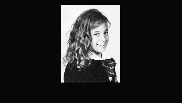 Ein Schwarzweißporträt eines lächelnden Mädchens mit lockigem Haar.