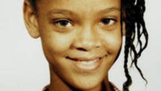 Ein Porträt der jungen Rihanna mit geflochtenen Zöpfen und einem freundlichen Lächeln.