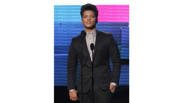 Bruno Mars steht in einem dunklen Anzug am Mikrofon.