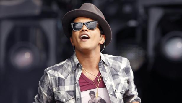 Bruno Mars tritt mit Hut und Sonnenbrille auf einer Bühne auf.
