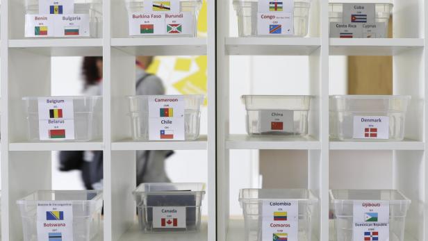 Ein Regal mit durchsichtigen Behältern, die mit Länderflaggen beschriftet sind.