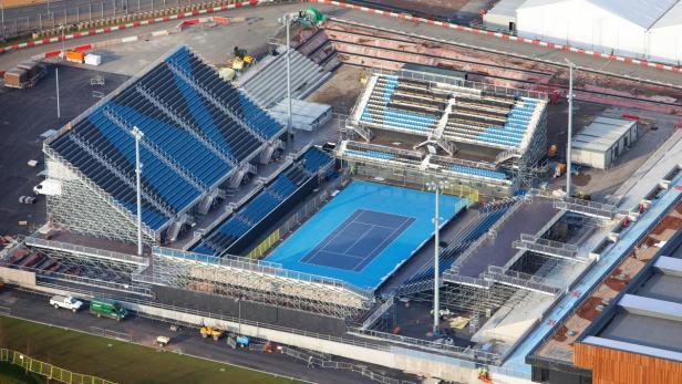 Luftaufnahme eines Tennisplatzes mit blauen Spielfeldern und temporären Tribünen.