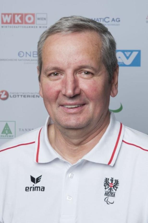 Ein Mann mit grauem Haar trägt ein weißes Poloshirt mit dem österreichischen Wappen.