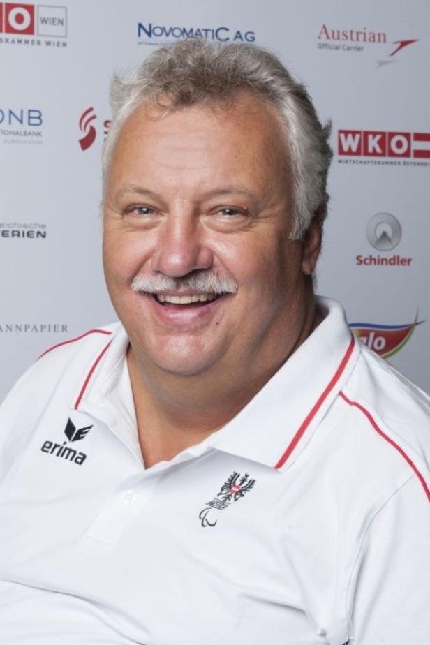 Ein lächelnder Mann mit Schnurrbart trägt ein weißes Poloshirt mit österreichischem Logo.