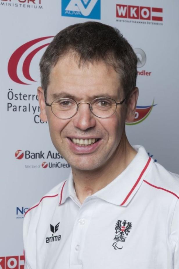 Ein lächelnder Mann mit Brille und einem Poloshirt mit dem österreichischen Logo.