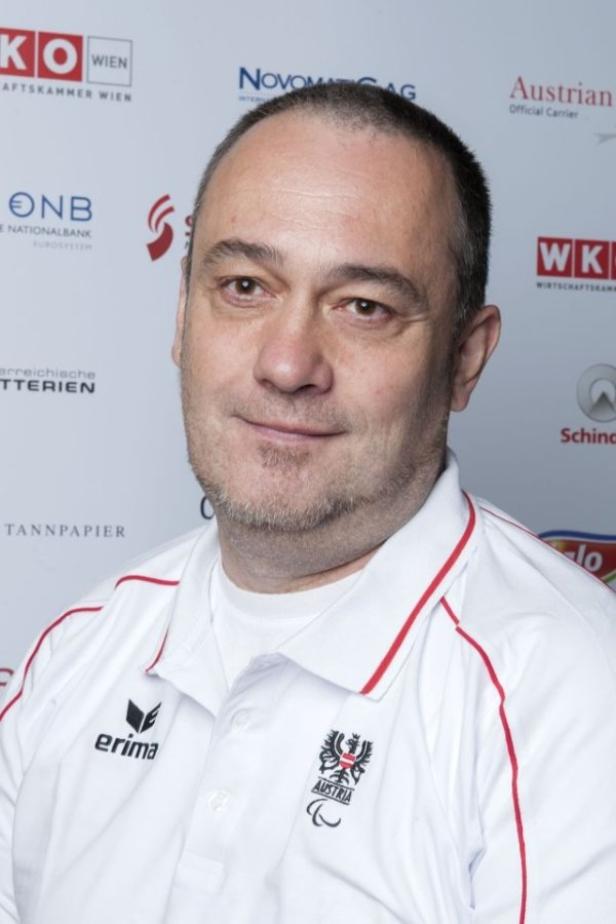 Ein Mann in einem weißen Hemd mit dem österreichischen Logo vor einem Sponsorenhintergrund.
