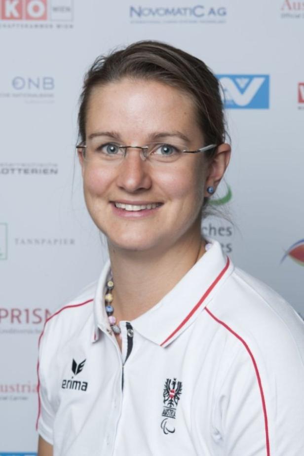 Eine lächelnde Frau mit Brille und Sportbekleidung vor einem Sponsorenhintergrund.