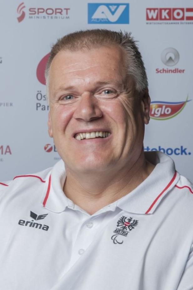 Ein lächelnder Mann im Poloshirt des österreichischen Behindertensportverbands vor einem Sponsorenhintergrund.