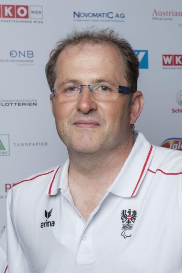 Ein Mann mit Brille und einem Poloshirt mit dem österreichischen Logo vor einem Sponsorenhintergrund.