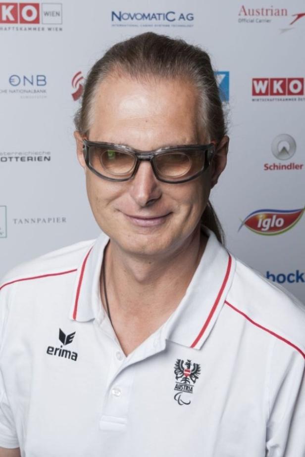 Ein Mann mit Brille und österreichischer Sportbekleidung lächelt.