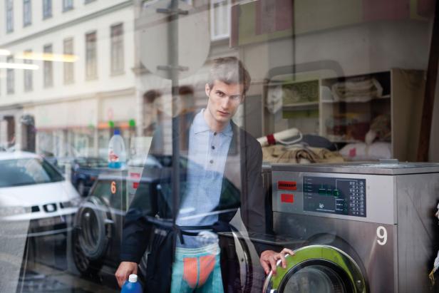 Ein Mann steht vor einem Waschsalon und hält eine Flasche Waschmittel.