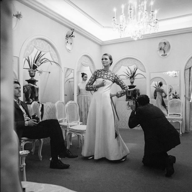 Eine Frau posiert in einem eleganten Kleid für einen Fotografen in einem opulenten Raum.