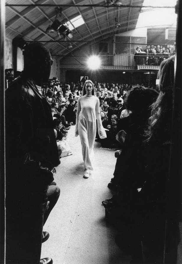 Eine Frau läuft in einem langen Kleid über einen Laufsteg vor Publikum.
