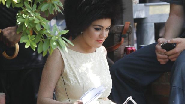 Lindsay Lohan mit Pelzmütze und hellem Kleid hält Papiere in der Hand.