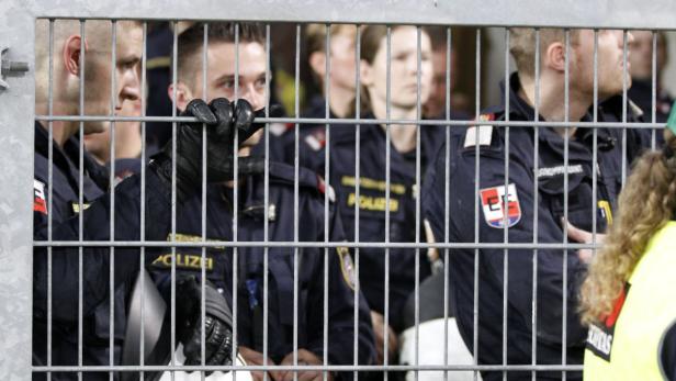 Eine Gruppe Polizisten steht hinter einem Metallzaun.