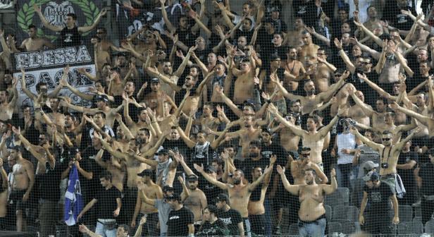 Eine große Gruppe von Fußballfans jubelt auf der Tribüne mit erhobenen Armen.