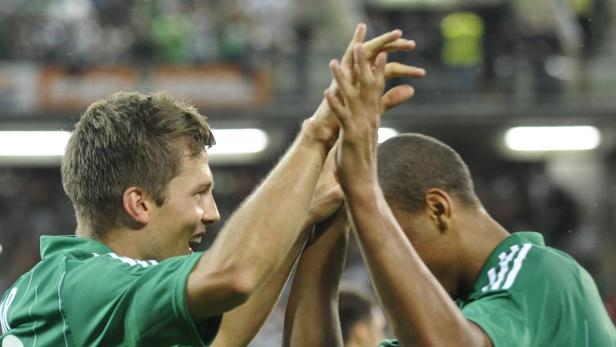 Zwei Fußballspieler in grünen Trikots feiern gemeinsam.